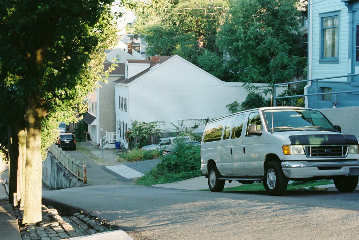 White service van parked at the curb of a leafy residential street