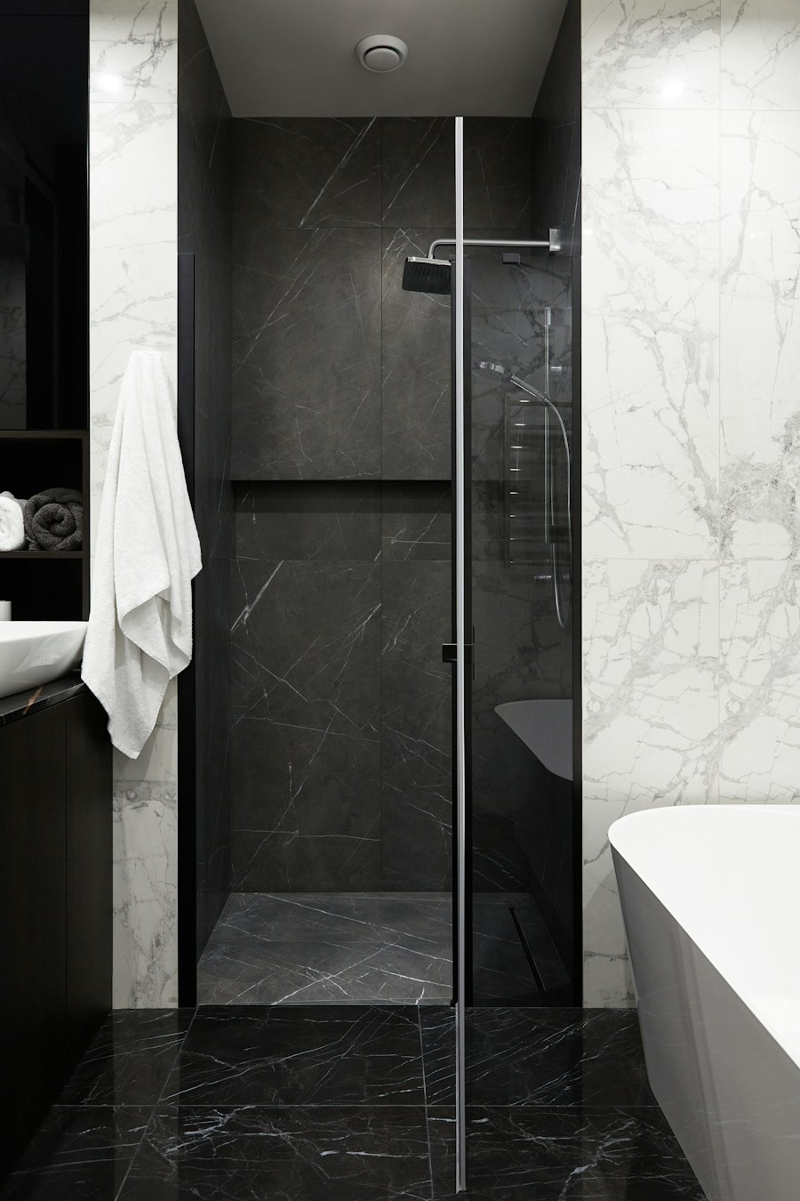 Finished walk-in shower lined with dark marble tile behind a glass screen