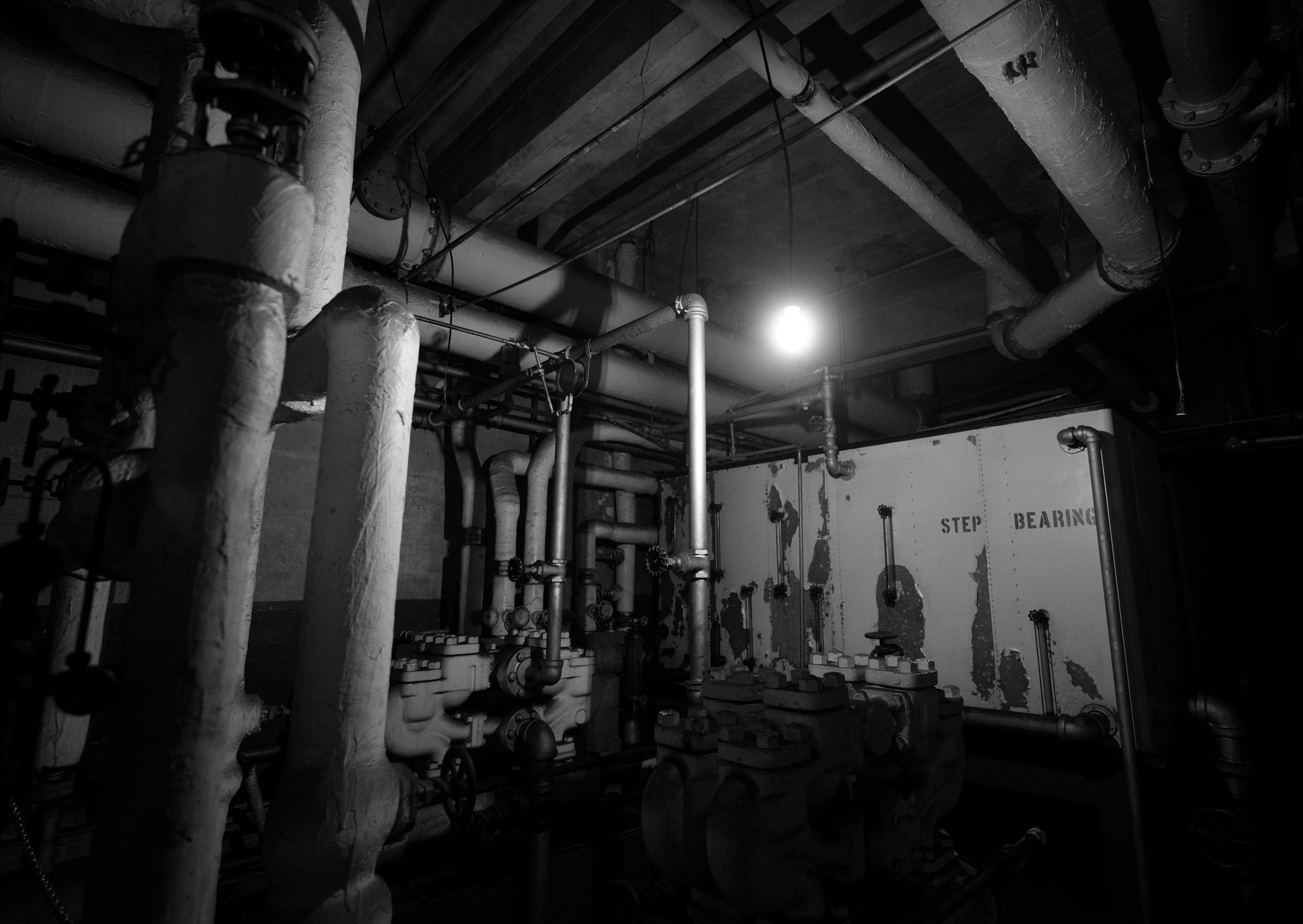 Pipes, valves and a work lamp in a dark boiler room