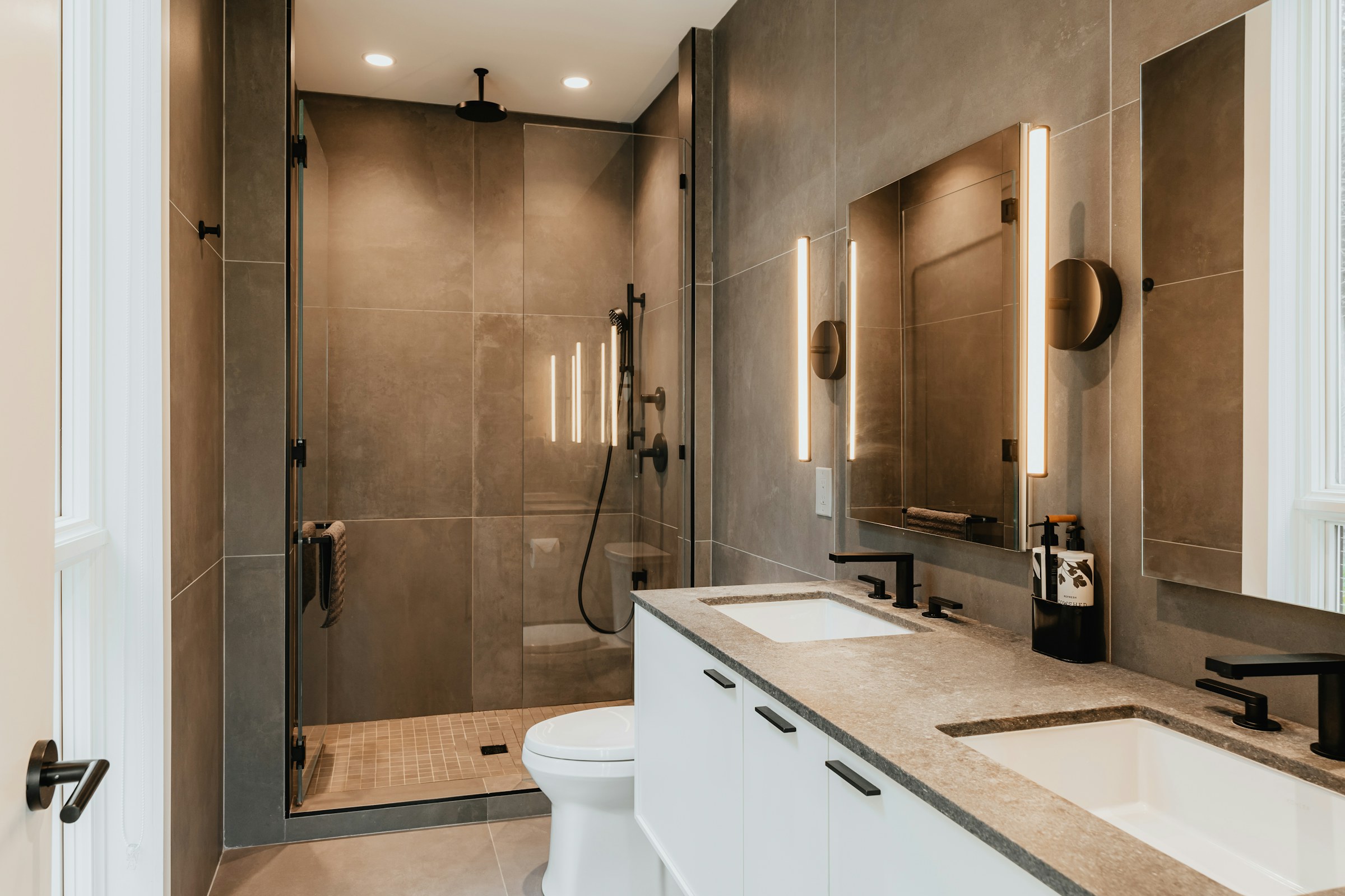 Finished bathroom with large grey tiles, a glass walk-in shower and a double vanity