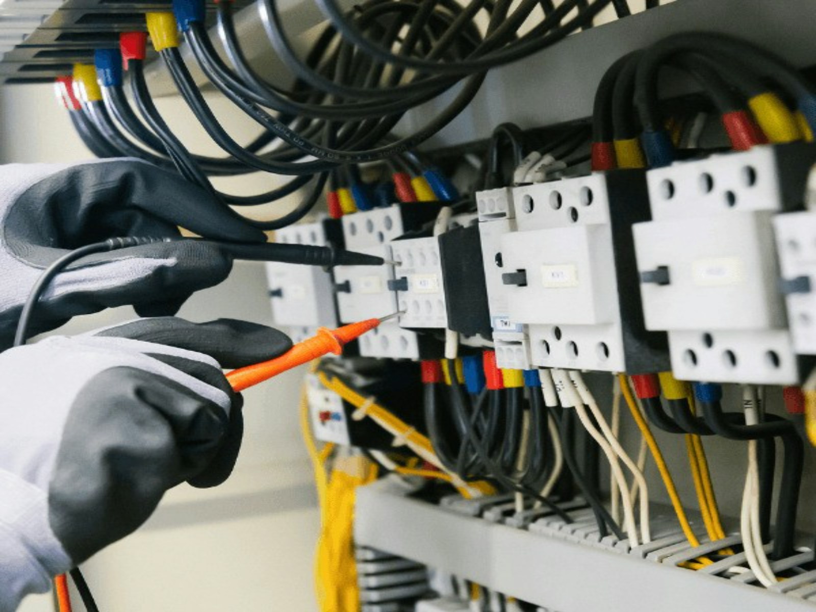 Electrician’s gloved hands wiring breakers inside an electrical panel