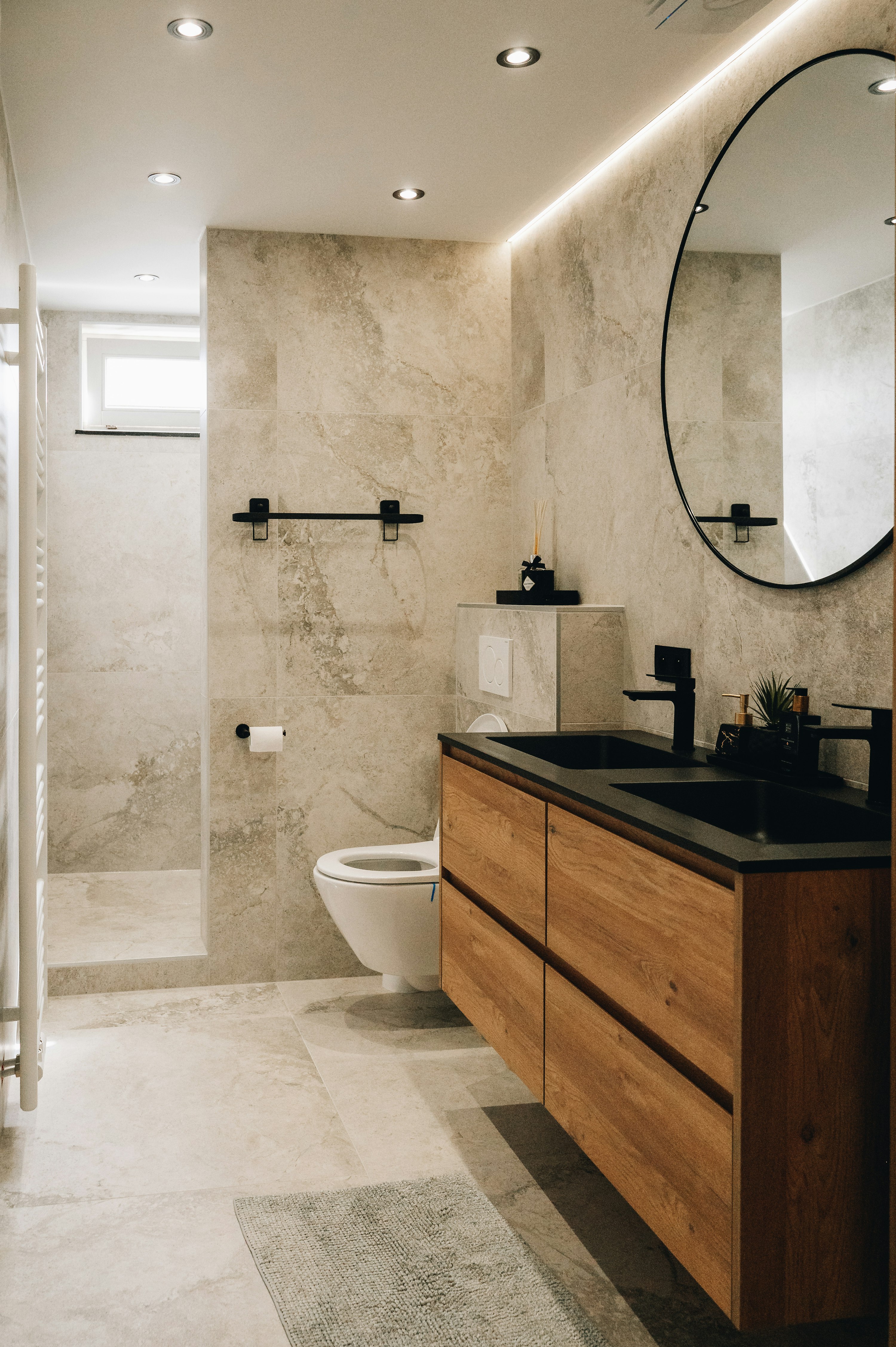 Finished bathroom remodel with a wood vanity, black fixtures and a round mirror